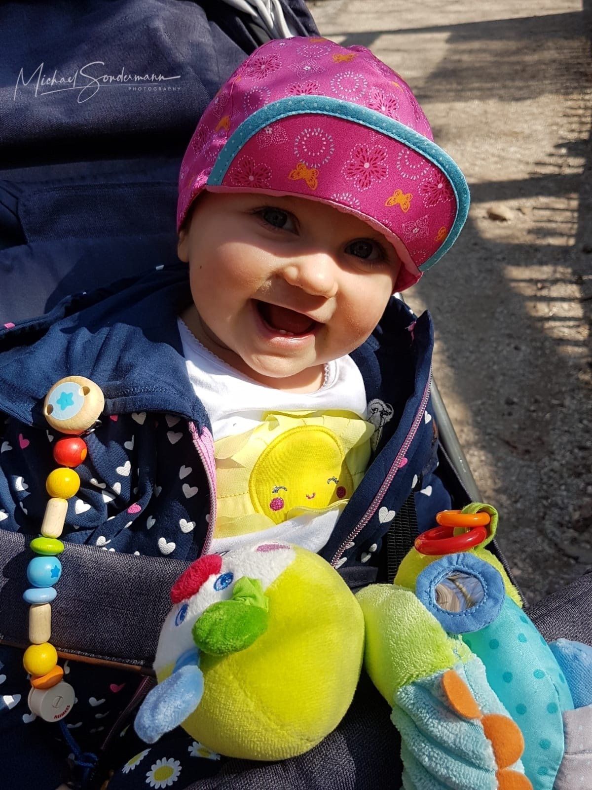 Ein junges Mädchen sitzt im Sonnenschein im Kinderwagen und ist am lachen.