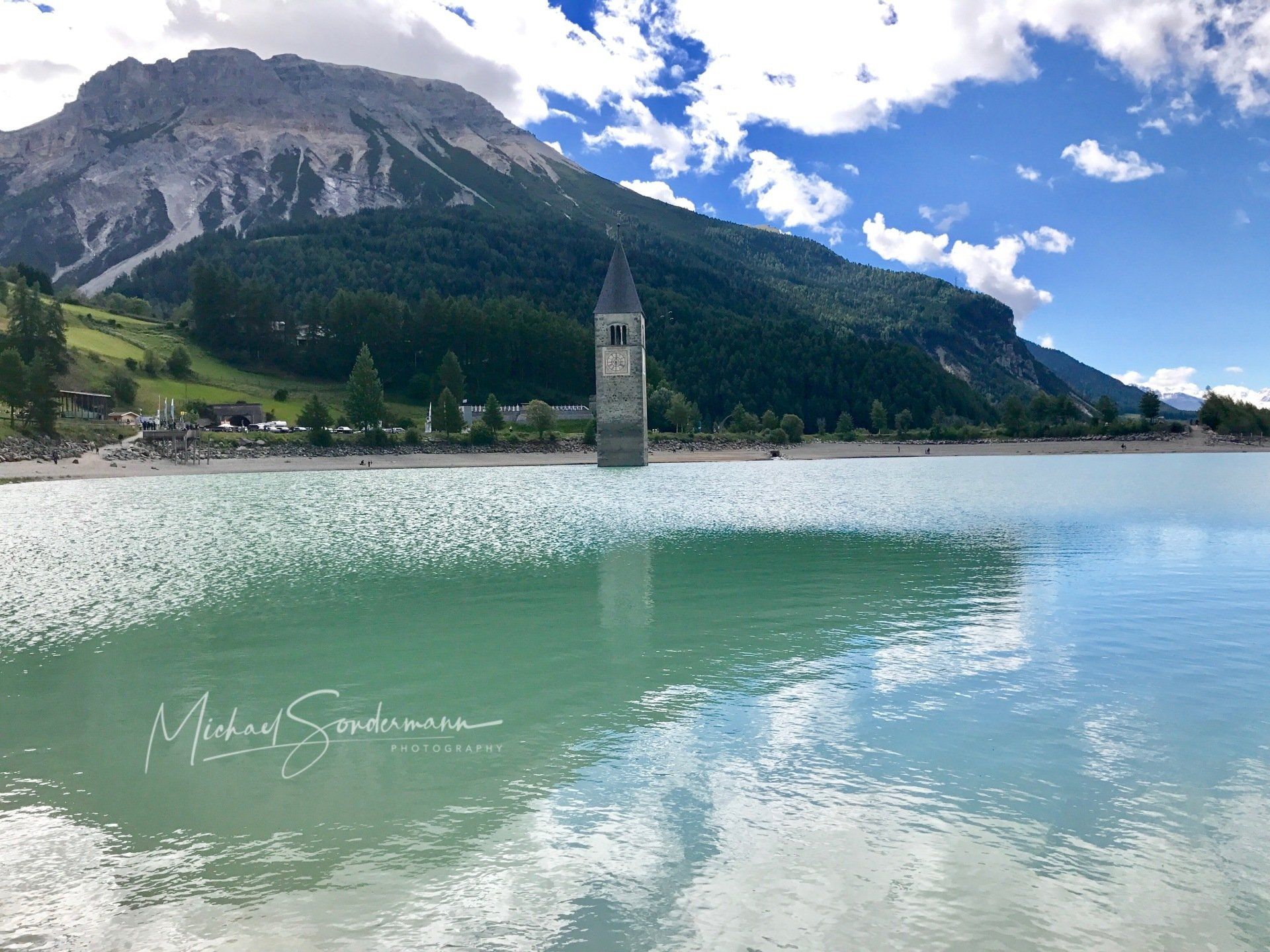 Ein Blick auf den schönen Lago di Resia in Italien mit türkisfarbenen Wasser und einen im See stehenden alten Kirchturm.