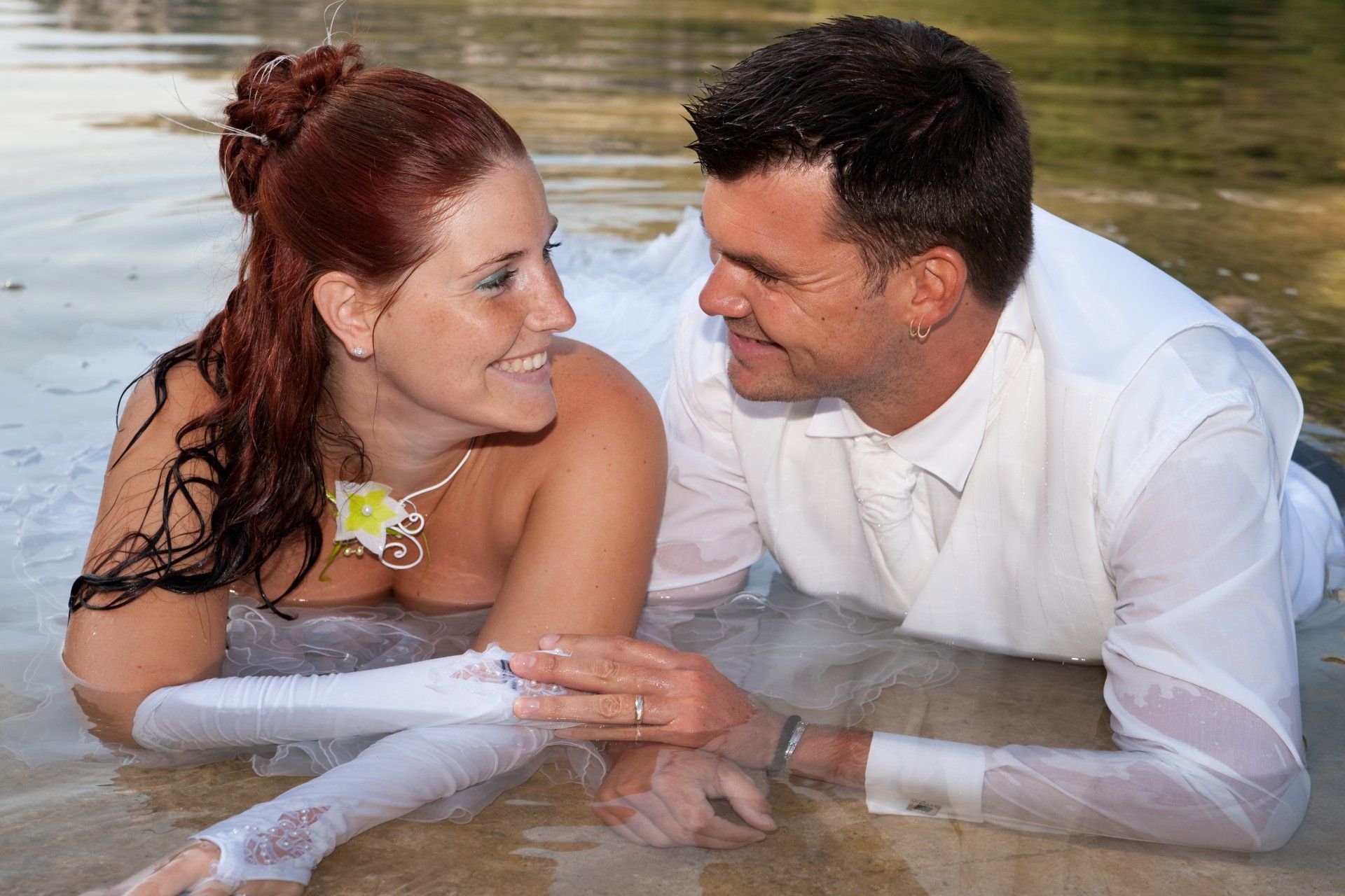 Braut und Bräutigam liegen im Wasser und schauen einander an.
