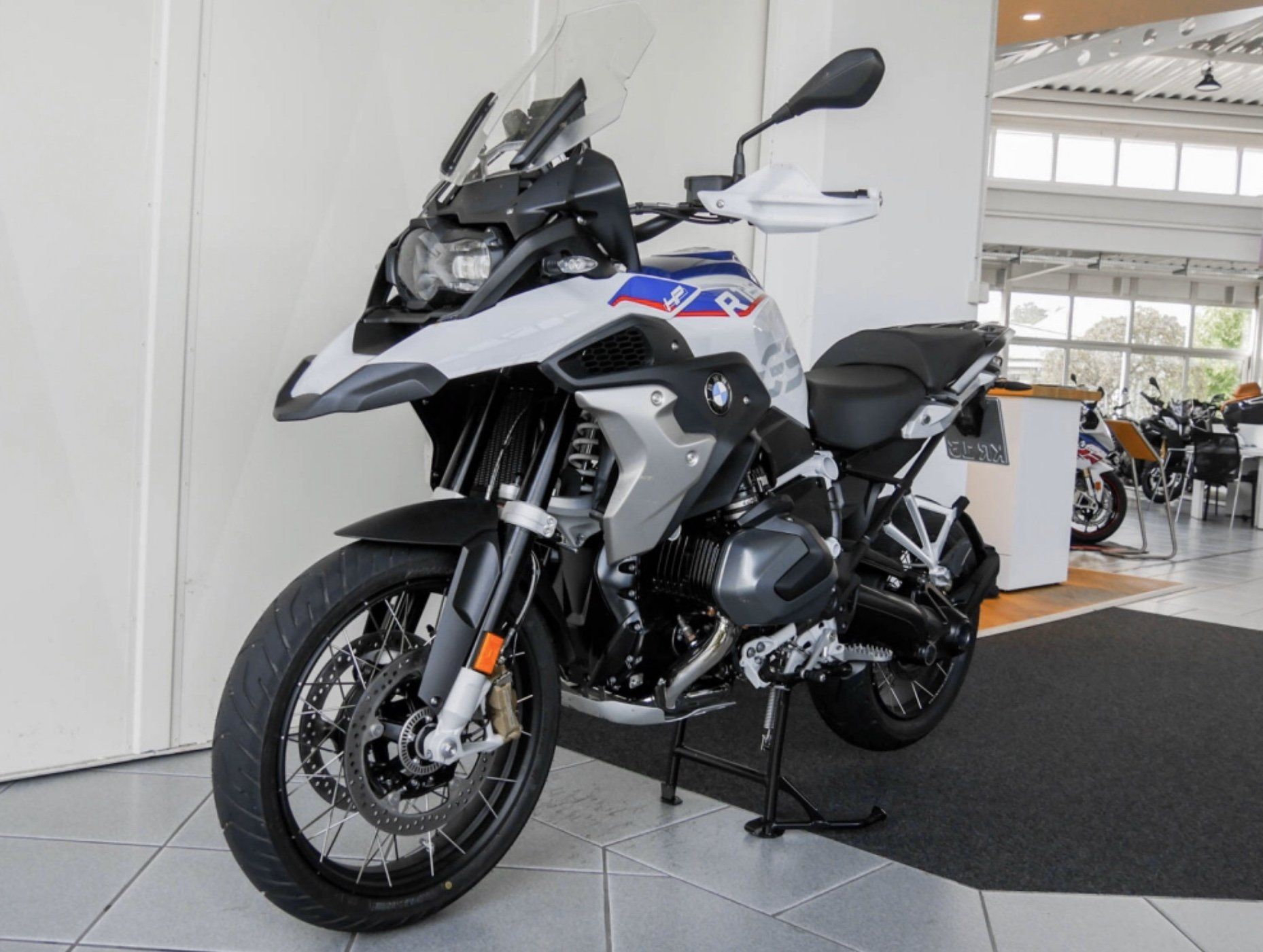 Ein Motorrad steht auf den Bodenfliesen in der Frontalansicht von vorne vor einer weißen Wand auf dem Ständer.