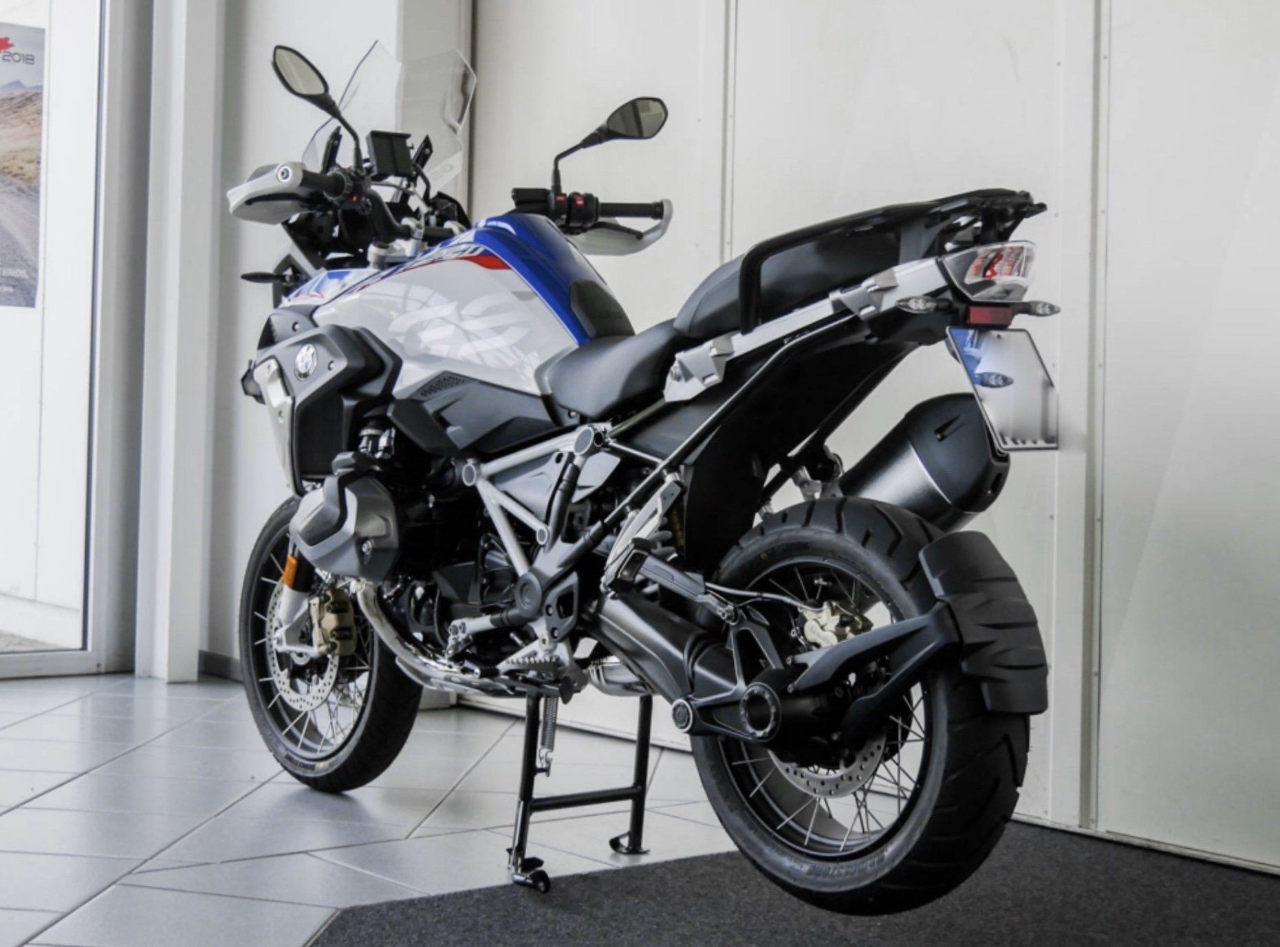 Ein Motorrad steht auf den Bodenfliesen in der Rückansicht von hinten vor einer weißen Wand auf dem Ständer.