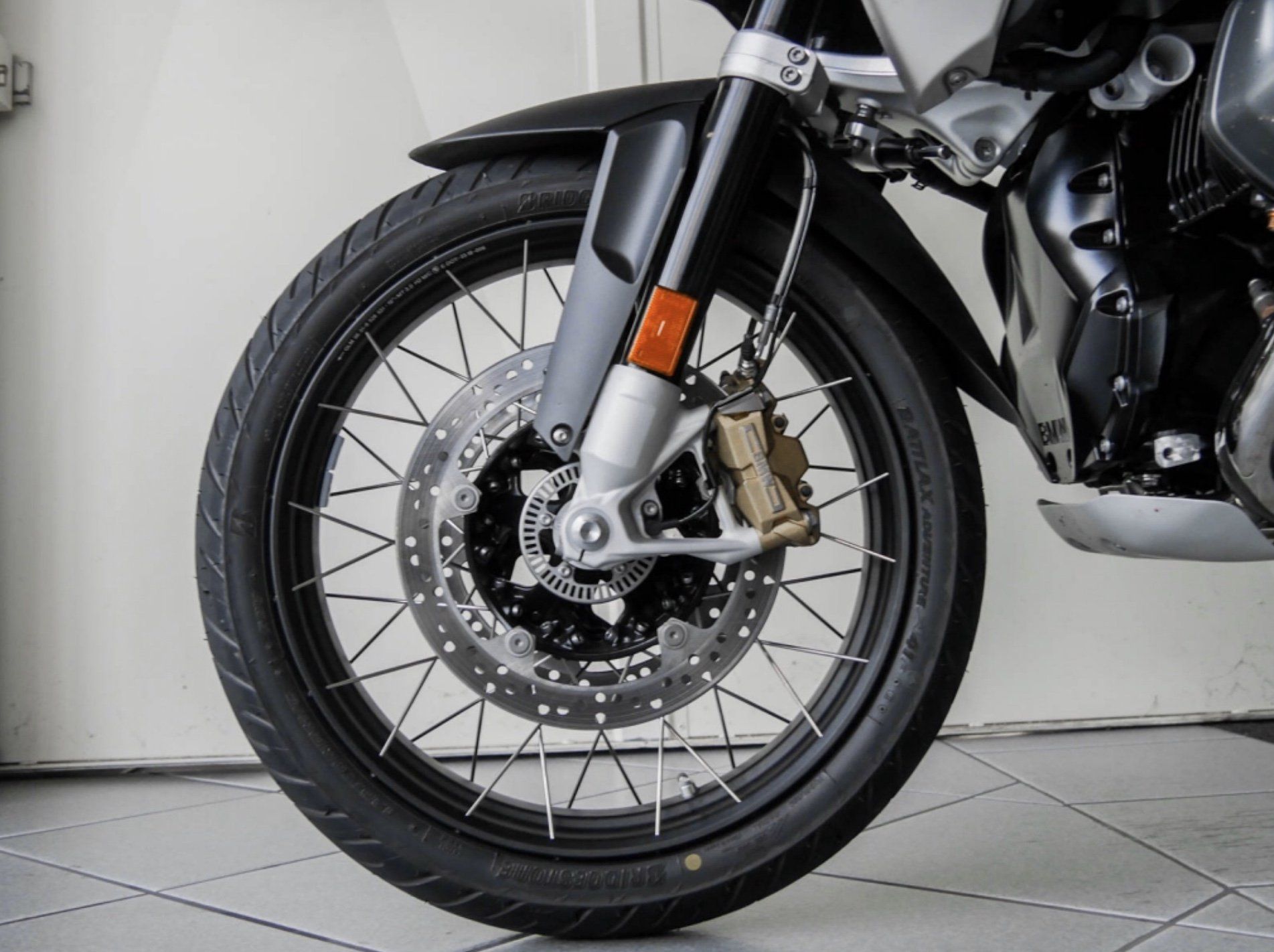 Ein Motorrad steht auf Bodenfliesen in der Sicht auf die vordere Felge vor einer weißen Wand auf dem Ständer.