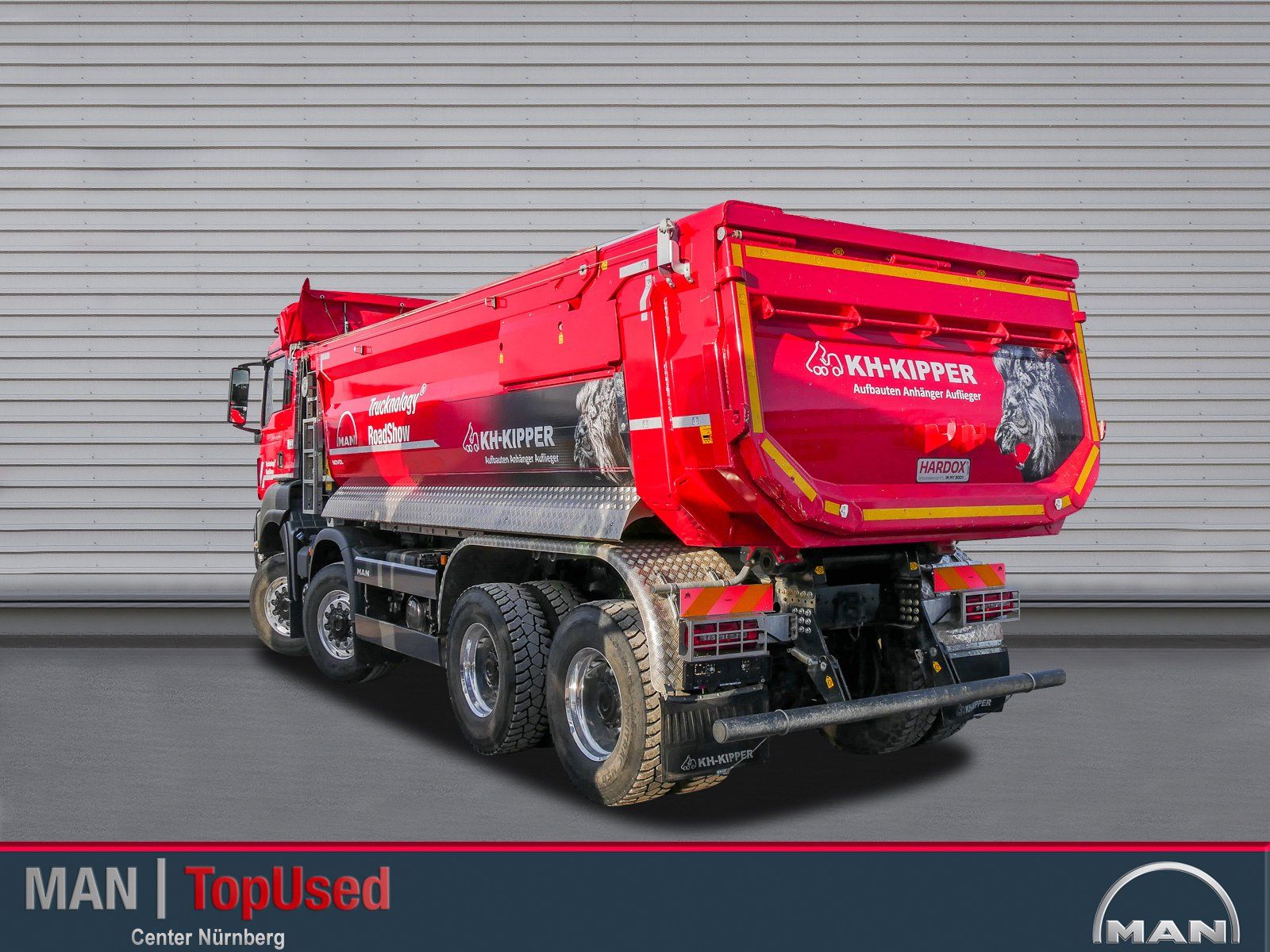 Ein großer roter 4 achsiger Truck von hinten links gesehen mit eingeschlagenen Vorderrädern vor einer geriffelten Wand.