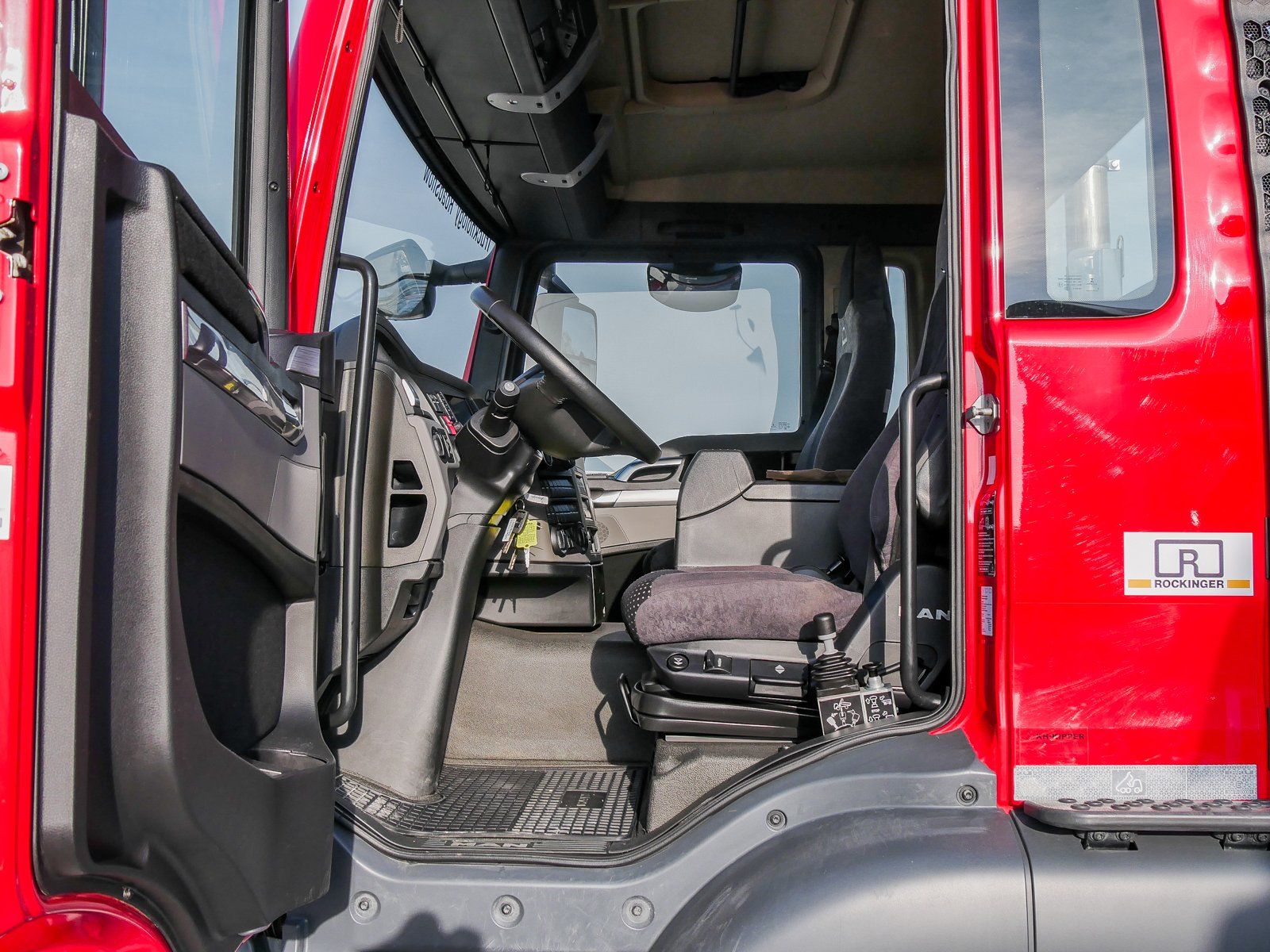 Ein großer roter 4 achsiger Truck von der Fahrerseite gesehen in den Fahrgastraum durch die offene Fahrertür.