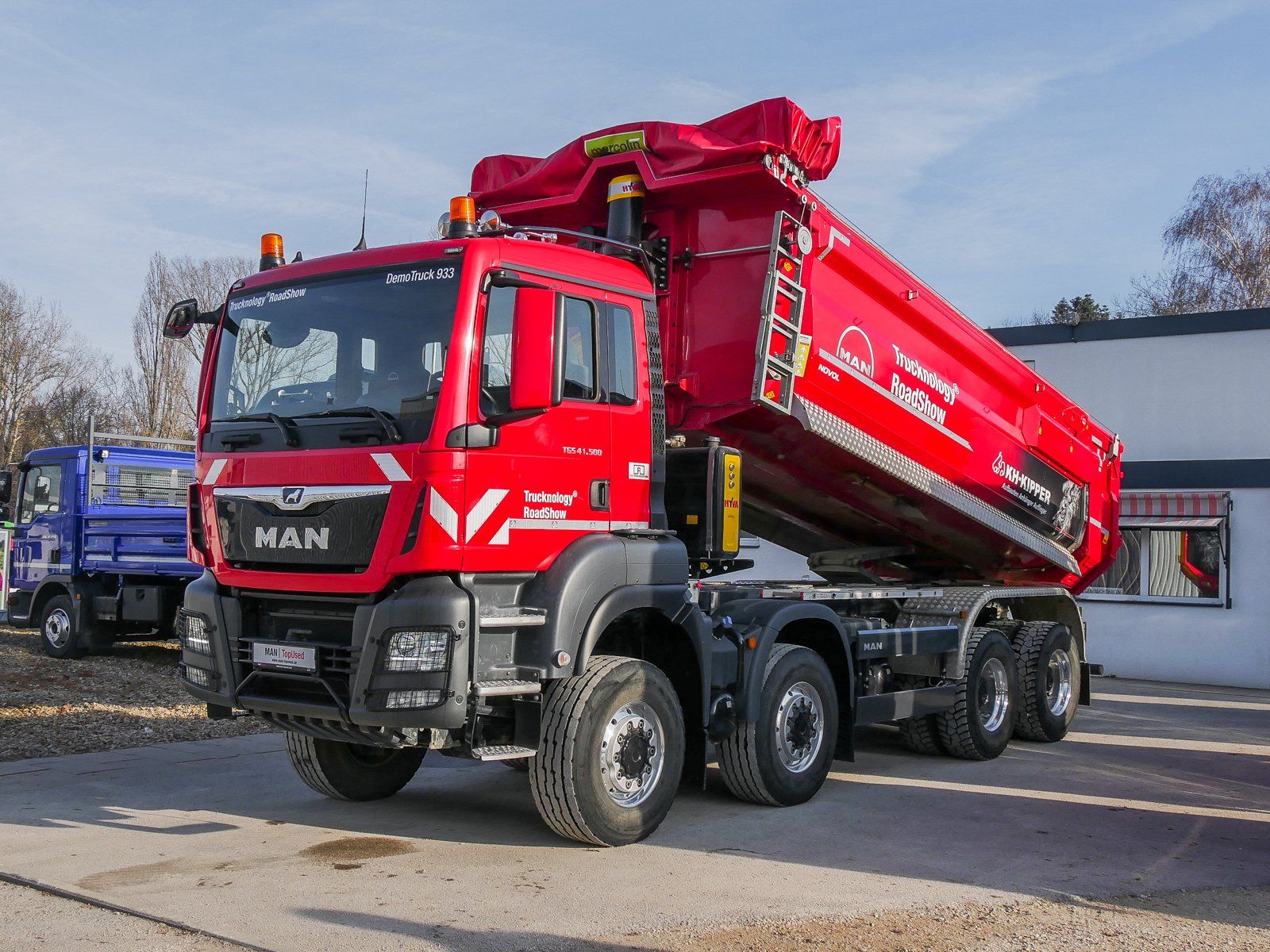 Ein großer roter 4 achsiger MAN Truck von vorne rechts gesehen mit einer hochgefahrenen Kippmulde.