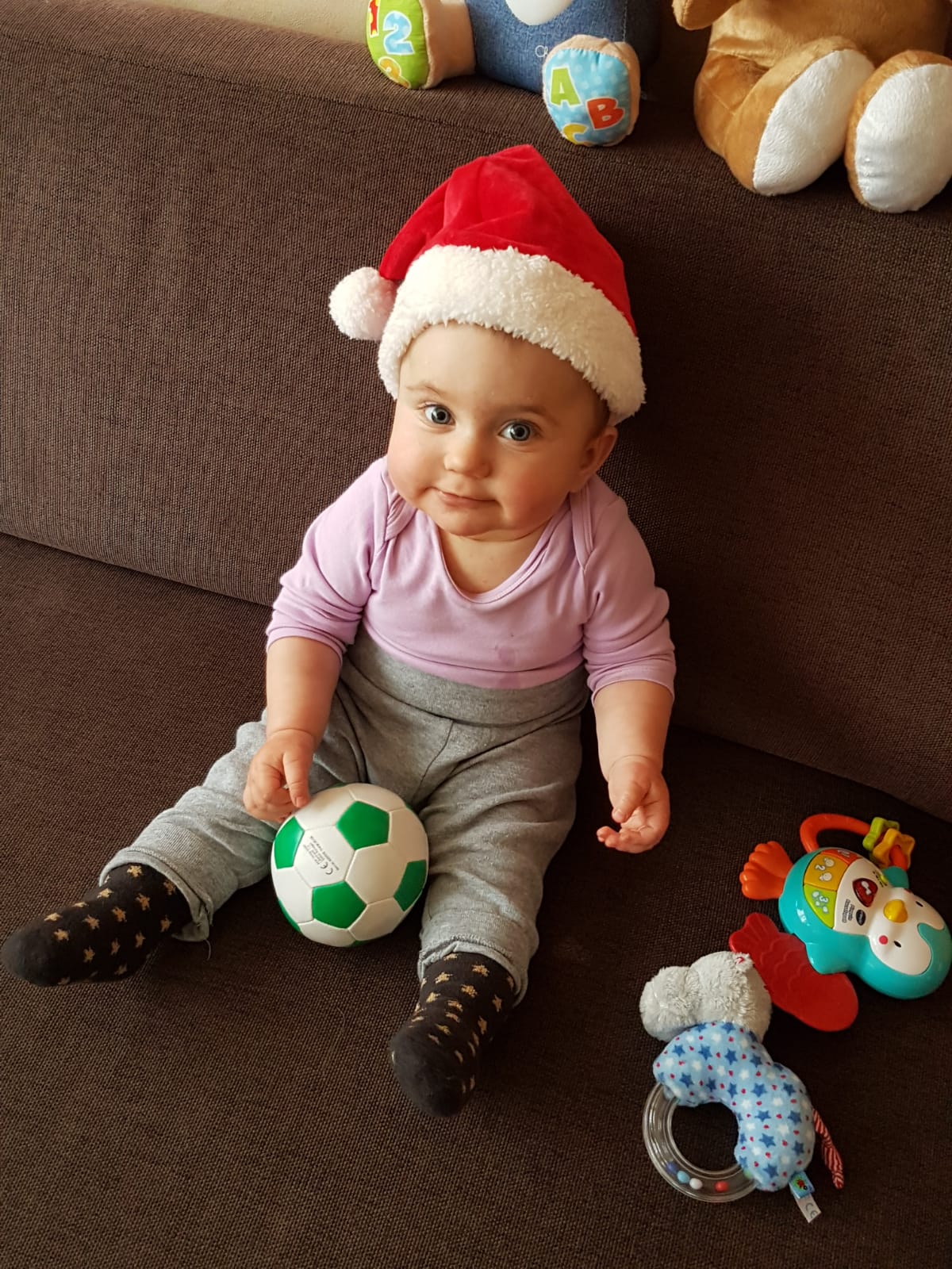 Ein Baby sitzt mit Nikolausmütze auf dem Sofa und lacht in die Kamera.