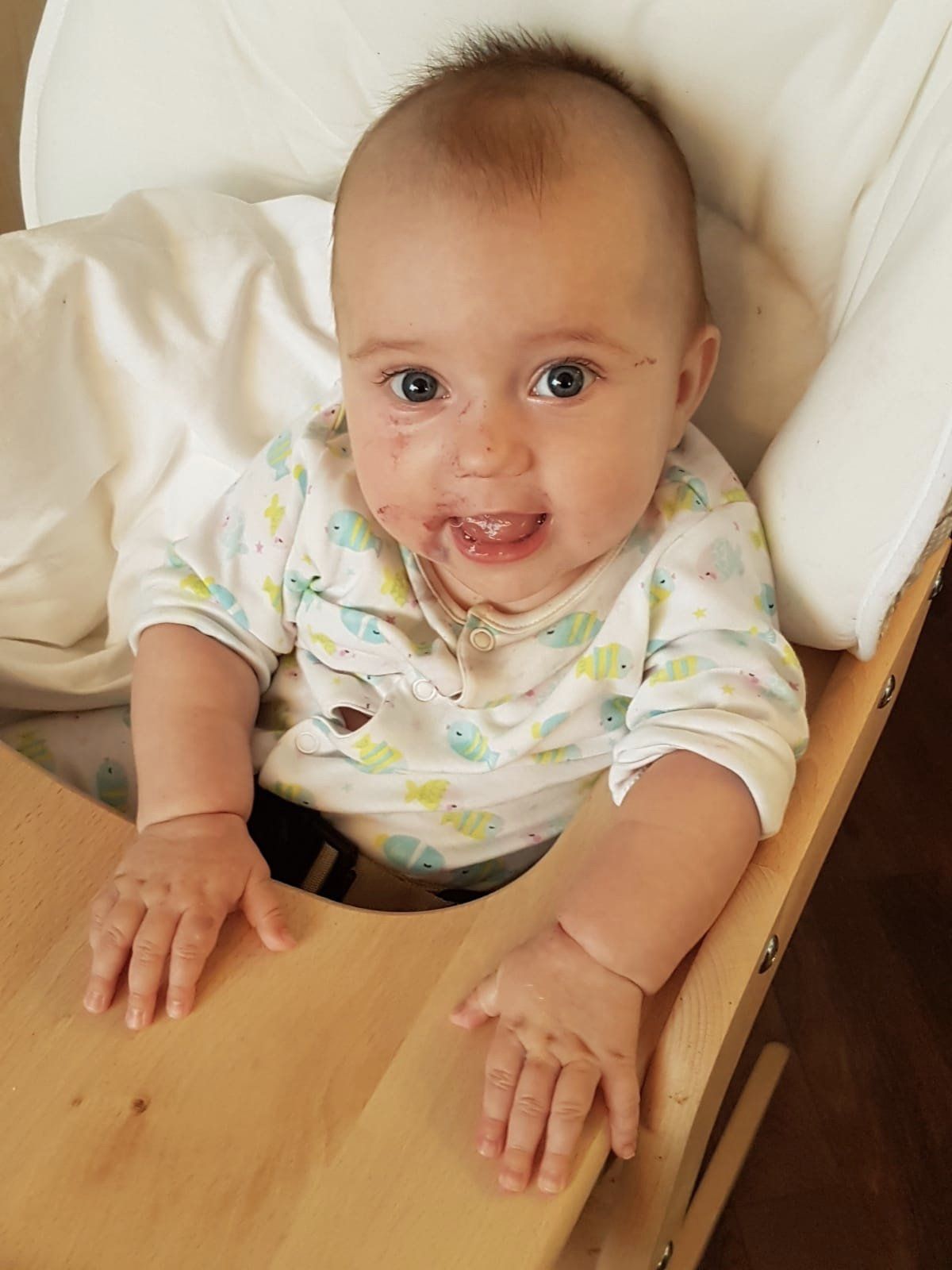 Ein Baby sitzt nach dem Essen im Hochstuhl und lacht in die Kamera.