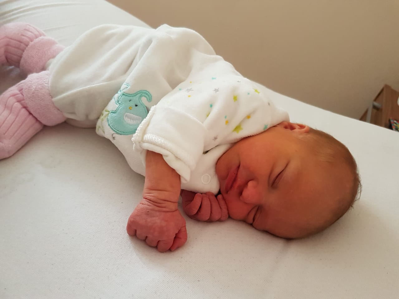 Ein Baby liegt im Strampler schlafend im Bett.