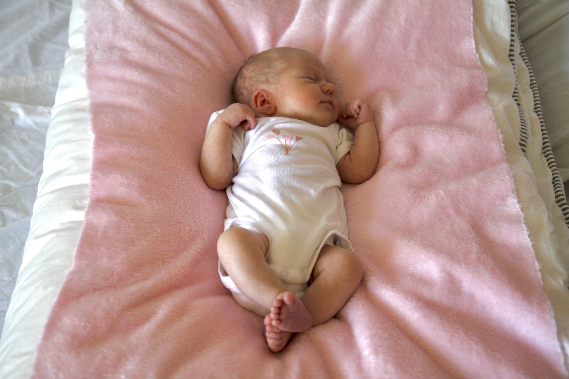 Ein Baby liegt im Strampler schlafend auf einer rosafarbenen Decke.