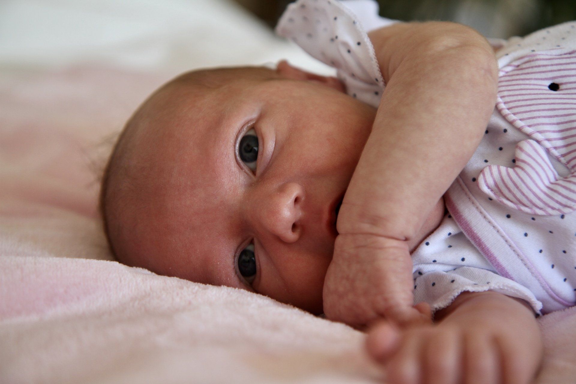 Ein Baby liegt wach auf dem Bett und guckt mit großen Augen in die Kamera.