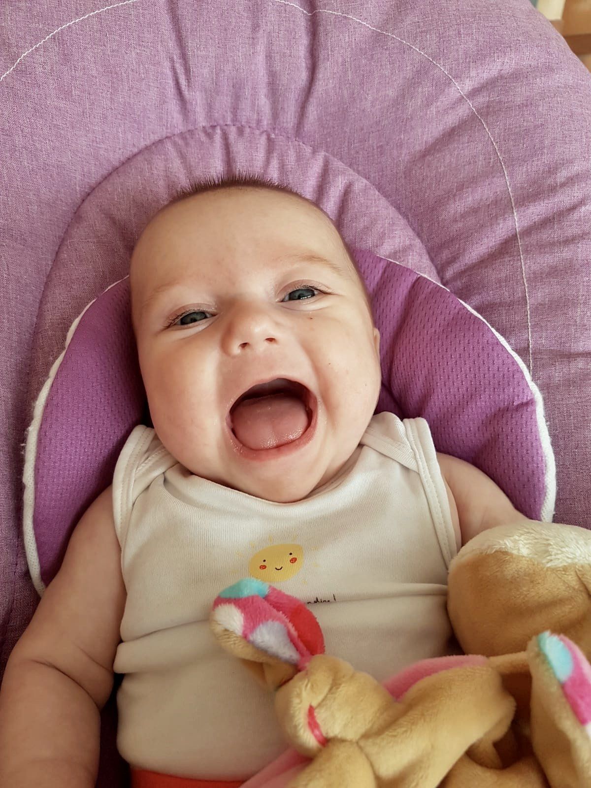 Ein Baby liegt in der Babyschale und lacht mit offenen Mund in die Kamera.