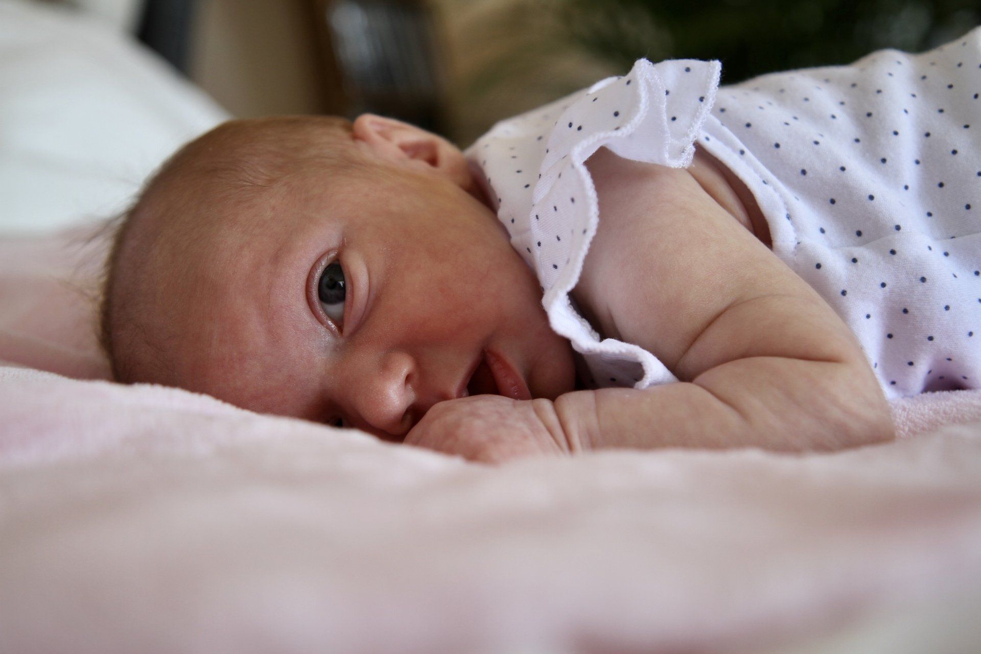 Ein Baby guckt mit großen Augen liegend auf dem Bett in die Kamera.