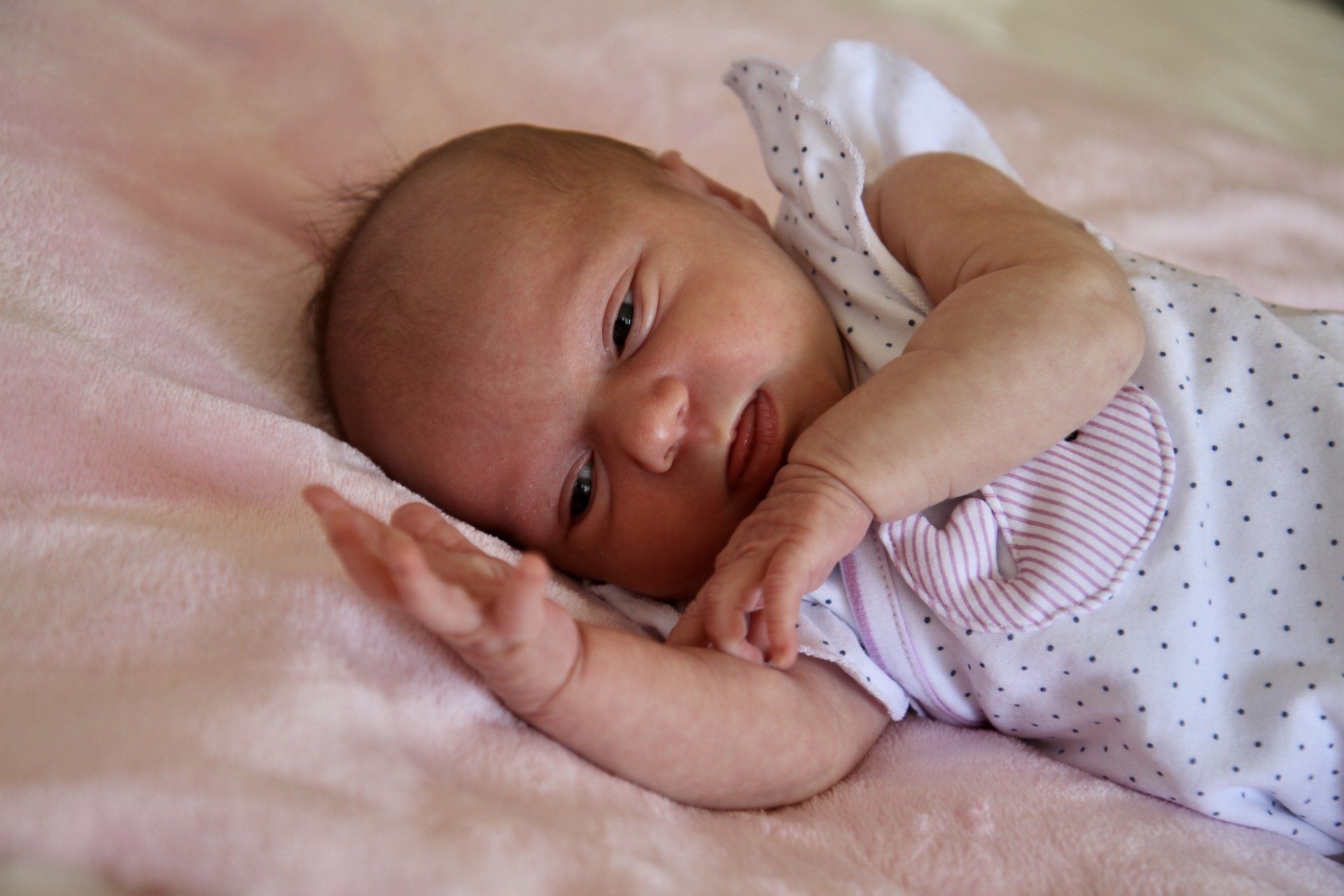 Ein Baby liegt im Bett und guckt in die Kamera.