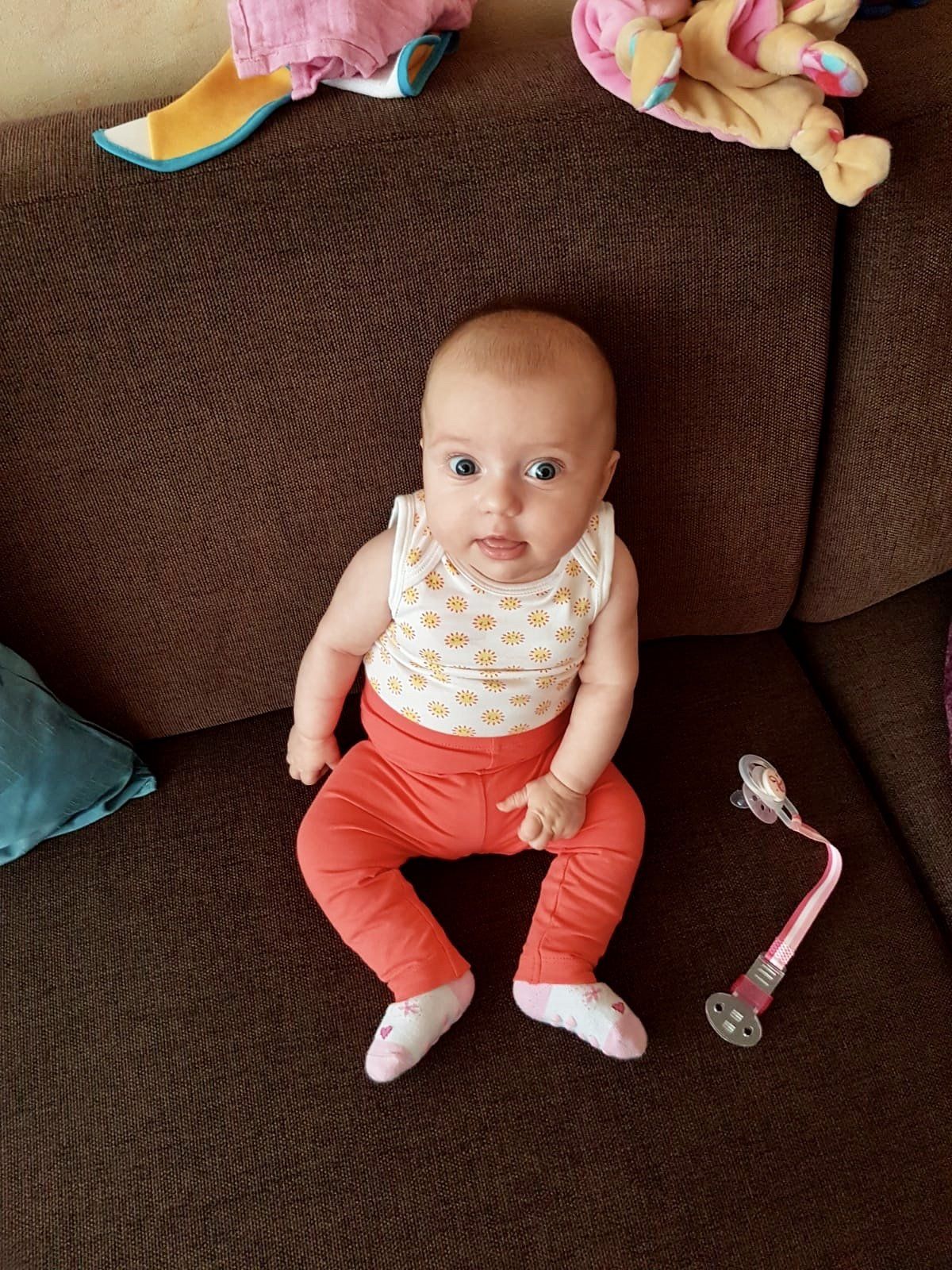 Ein Baby sitzt auf dem Sofa und guckt mit großen Augen in die Kamera.