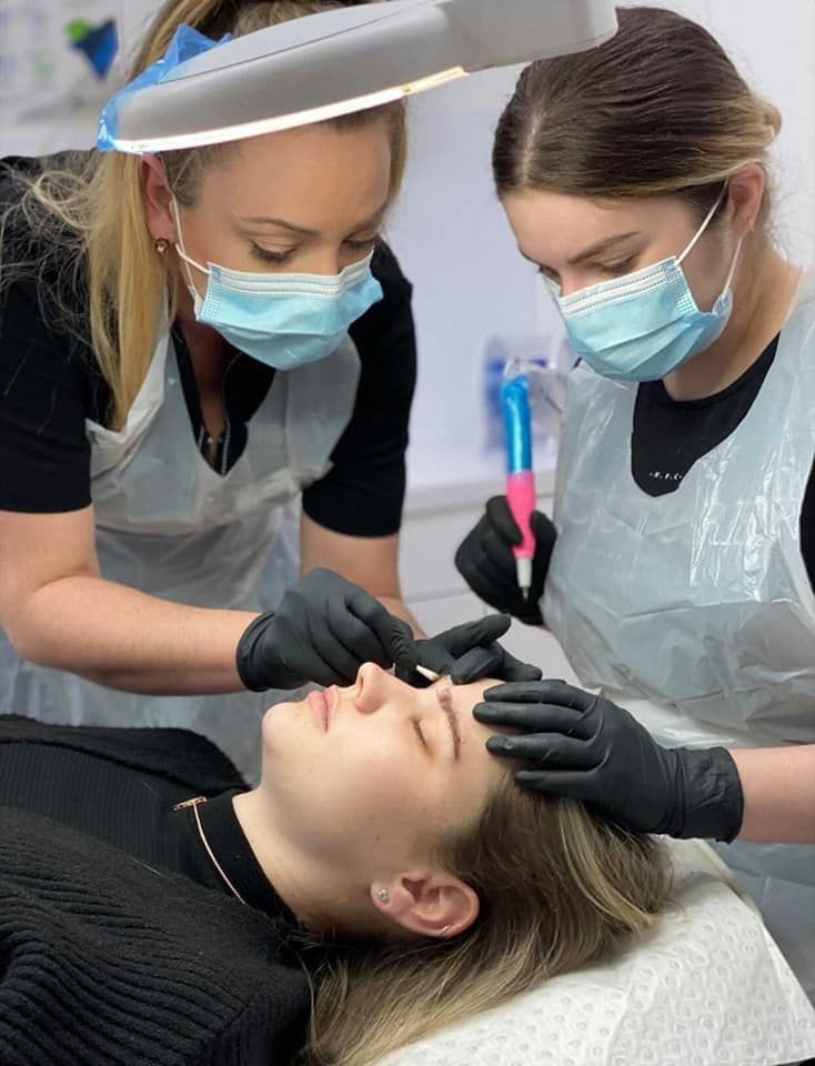 Two People in Masks Perform Eyebrow Microblading on a Client in a Clinic — Artisan Cosmetic Tattoo & Beauty in Worongary, QLD