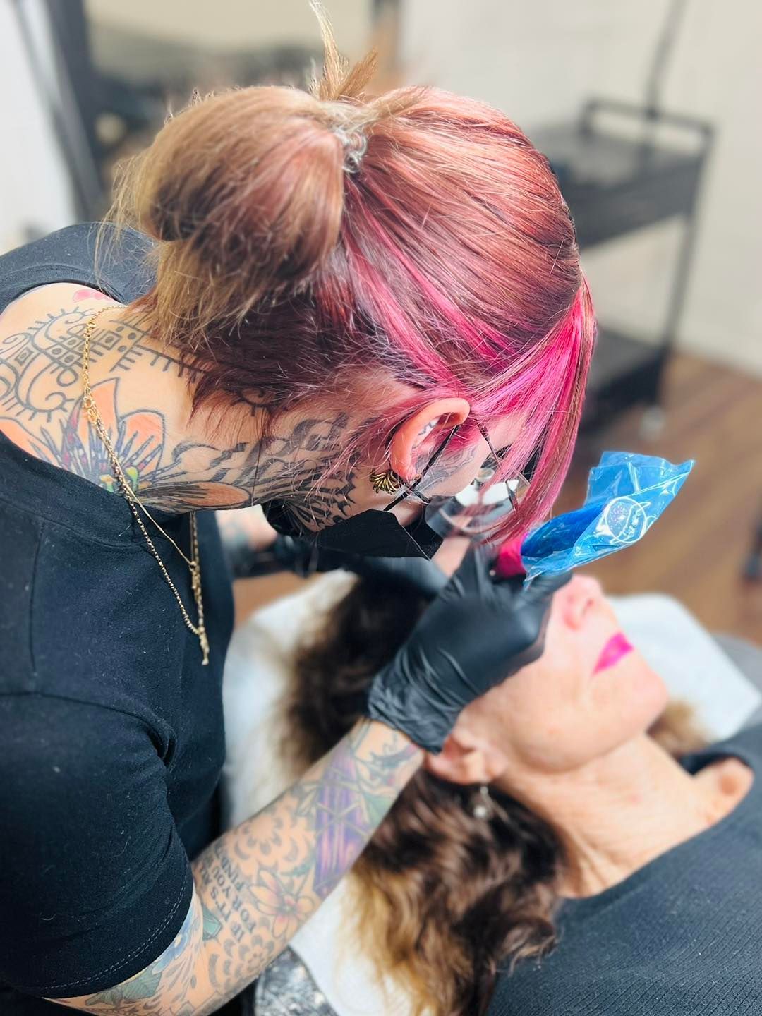 A Tattoo Artist with Pink Hair Working on A Client's Lip Tattoo — Artisan Cosmetic Tattoo & Beauty in Worongary, QLD