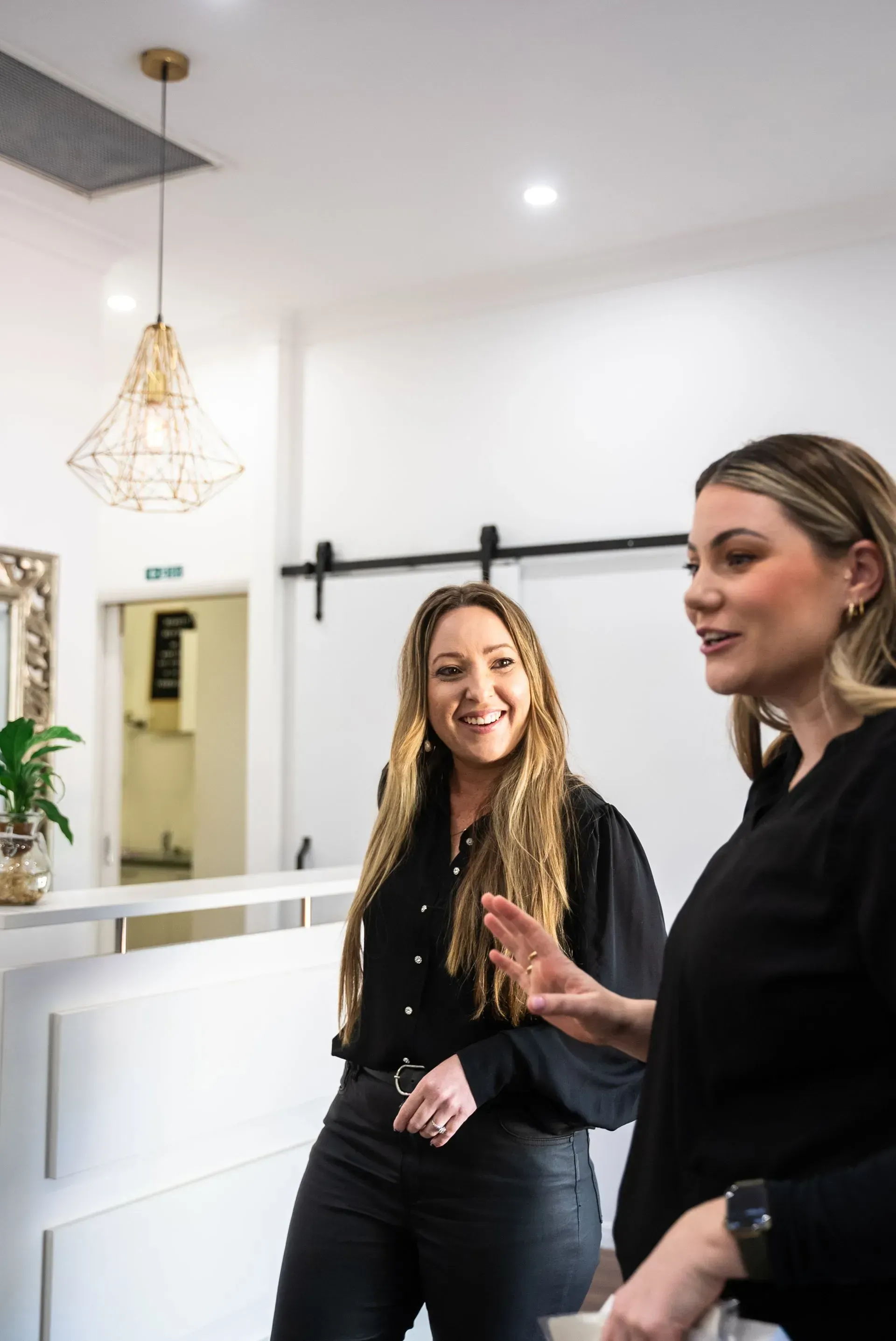 Two Women Talking in a White Room With a Reception Desk — Artisan Cosmetic Tattoo & Beauty in Worongary, QLD