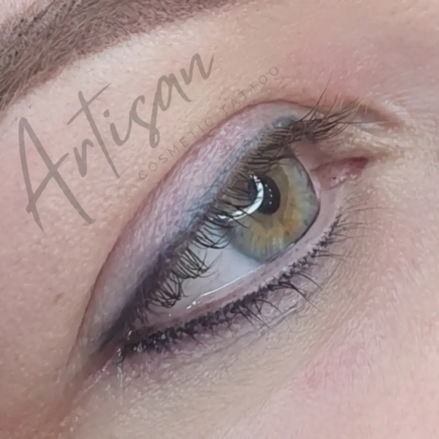 A close-up view of a green eye featuring subtle, dark cosmetic eyeliner tattooed along the upper lash line. — Artisan Cosmetic Tattoo & Beauty in Worongary, QLD