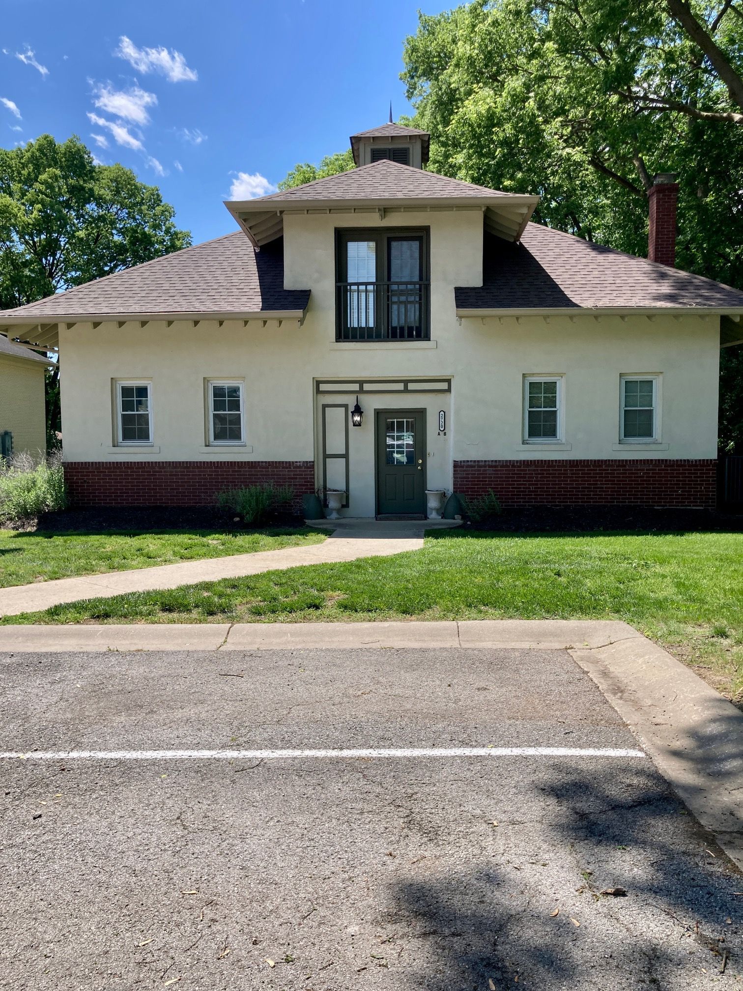 A white house with a black door is sitting next to a parking lot.