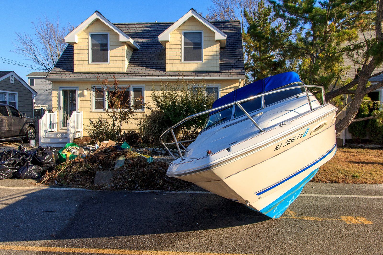 Boat leans against house, debris piles in yard, post-storm damage.