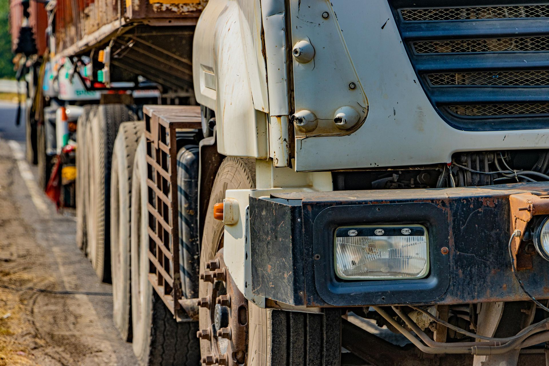 Close-up of a weathered, white semi-truck, its wheels and front details visible, parked on a dirt road.