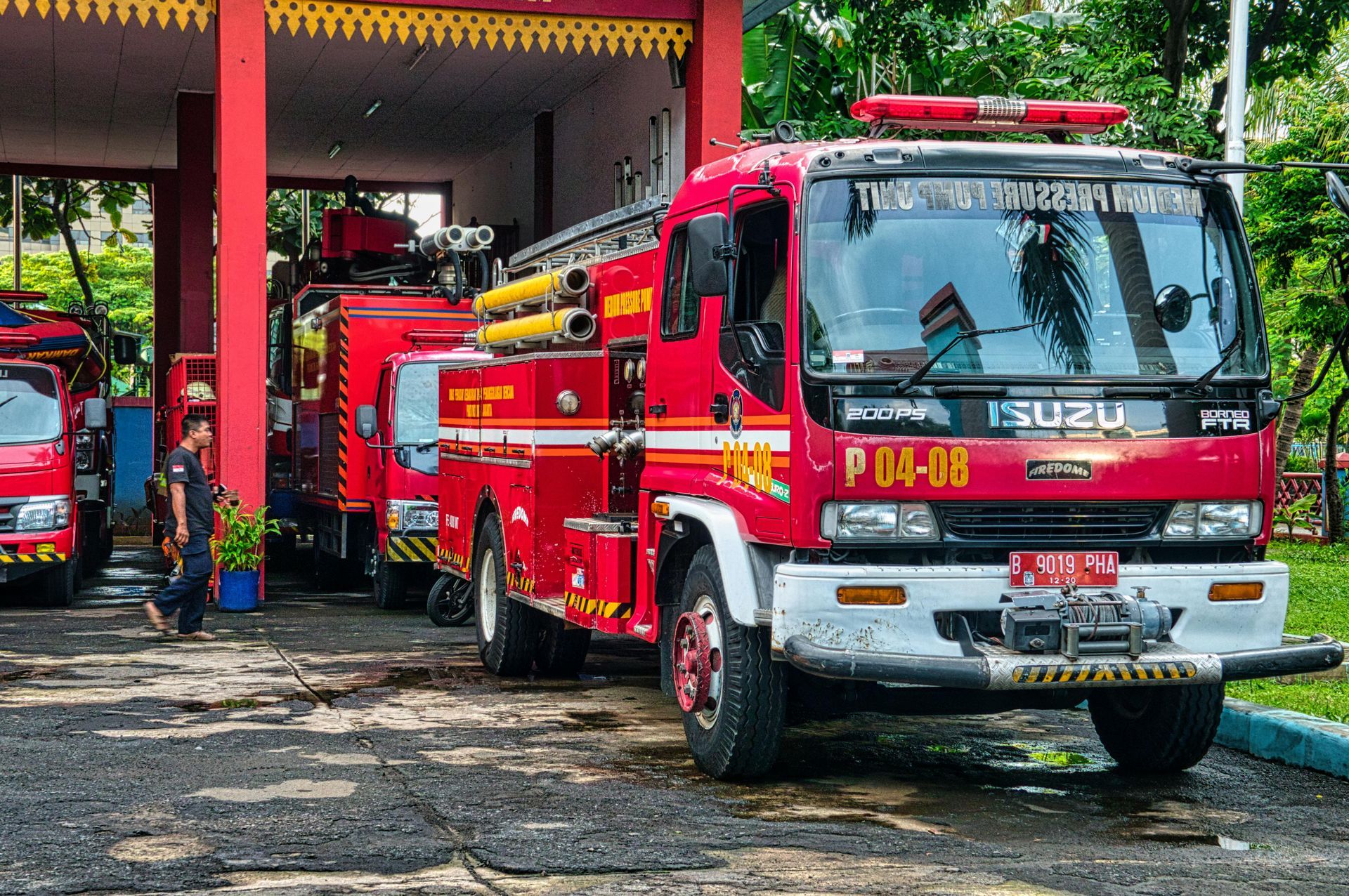 Red fire trucks parked under a red canopy, with a person standing nearby.