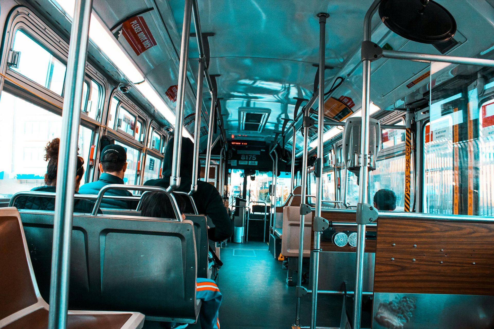 Interior of a public bus, with rows of seats, metal poles, and passengers seated.