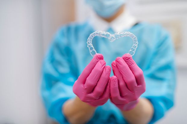 Una dentista tiene in mano un apparecchio ortodontico a forma di cuore.