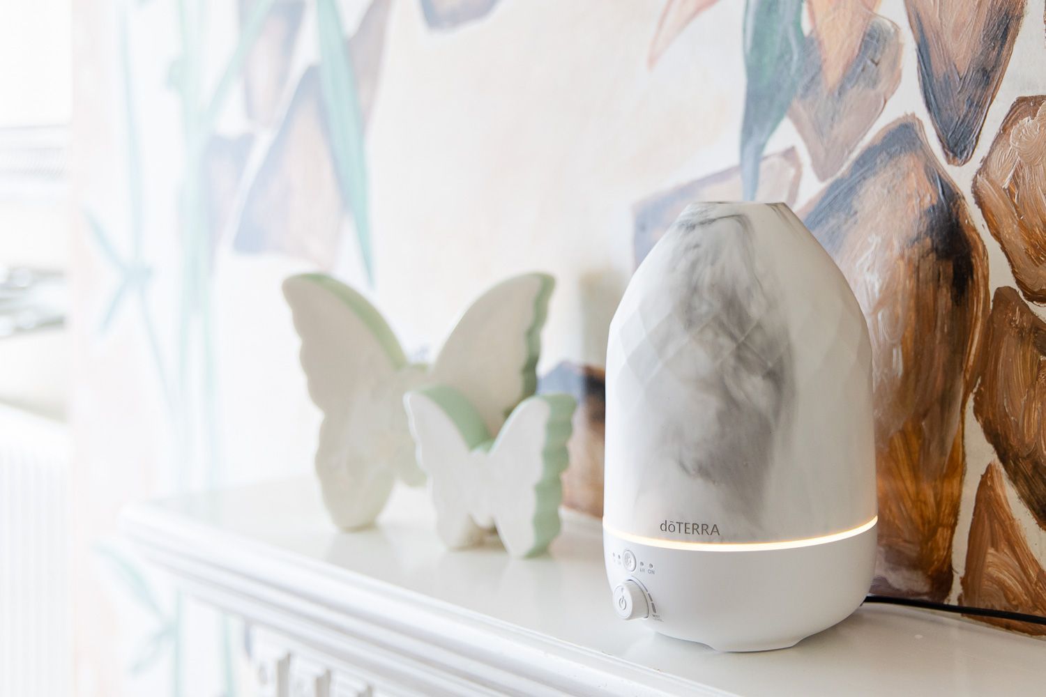 Auf einem Kaminsims steht neben Schmetterlingen ein weißer Diffusor für ätherische Öle.
