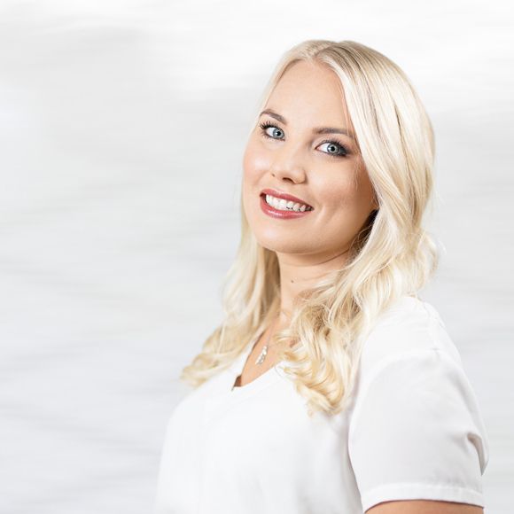 Eine Frau mit blondem Haar trägt ein weißes Hemd und lächelt.