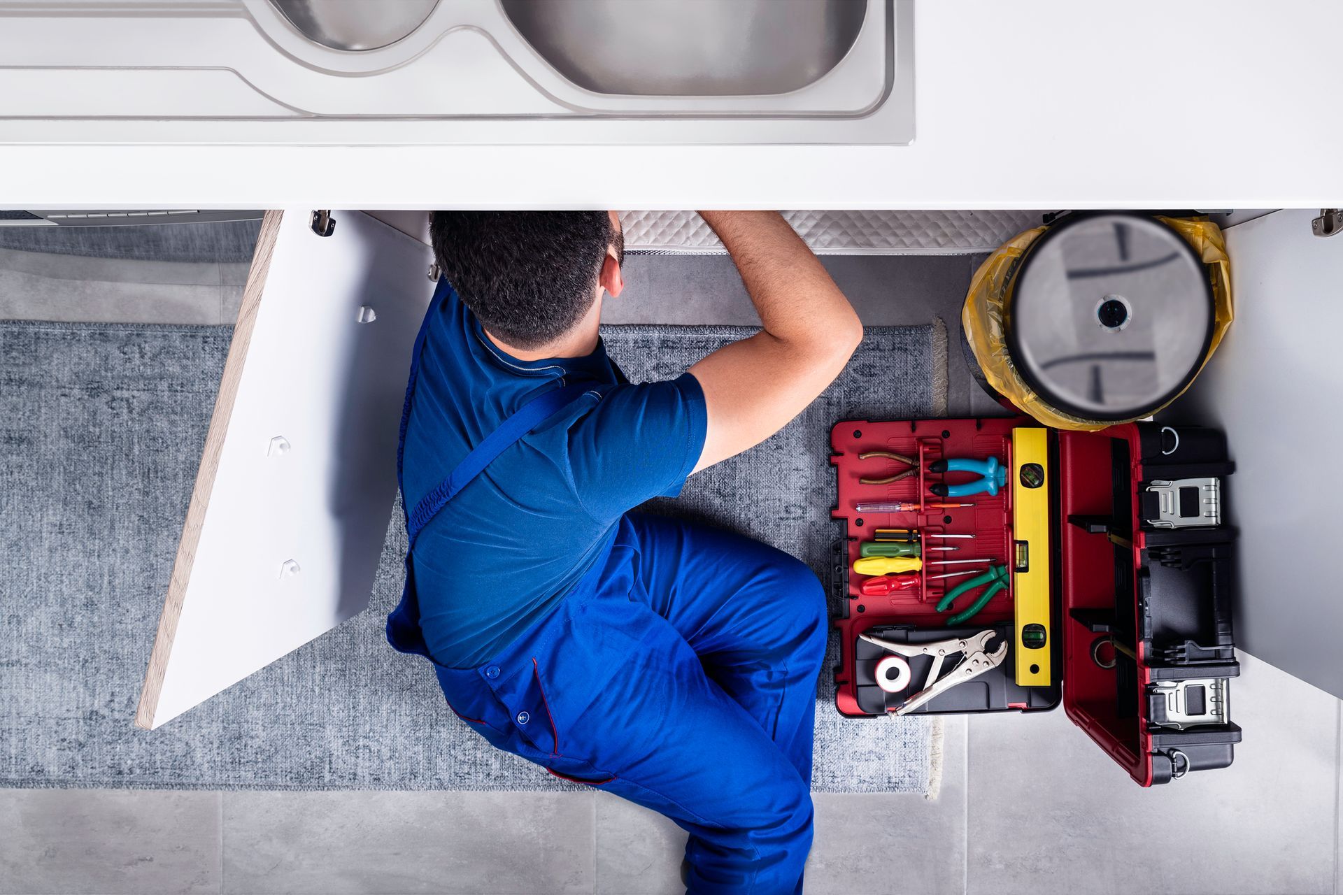 A plumber is working under a sink in a kitchen.