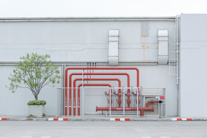 A white building with red pipes and a tree in front of it.