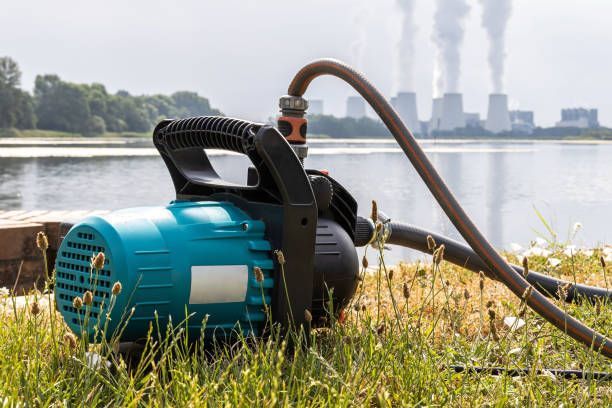 A water pump is sitting in the grass next to a lake.