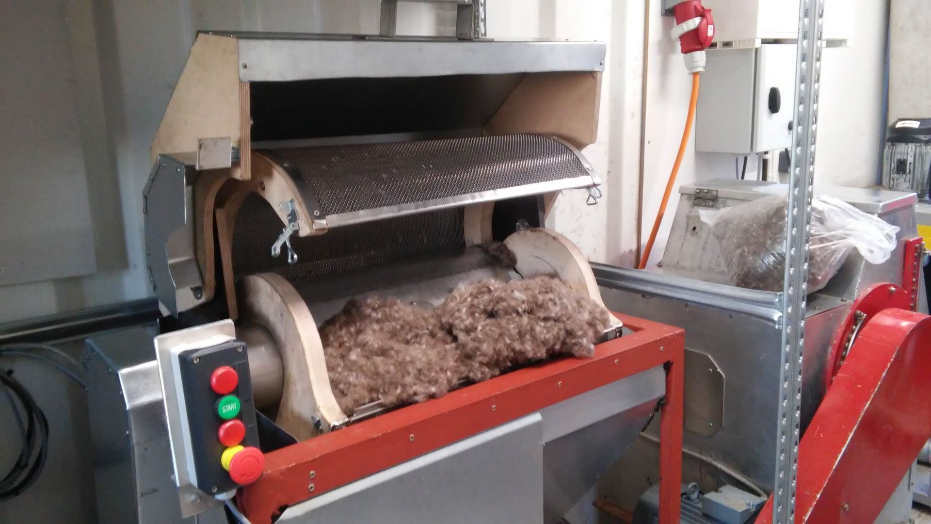 Industrial machine processing brown fibrous material. Red, green, and black control buttons.