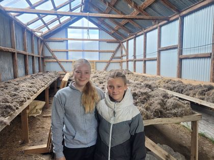 Two people in a greenhouse with piles of material on long tables.