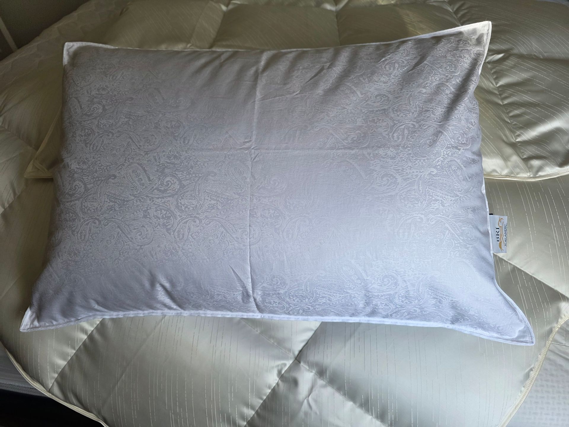 White rectangular pillow on a bed with light-colored bedding.