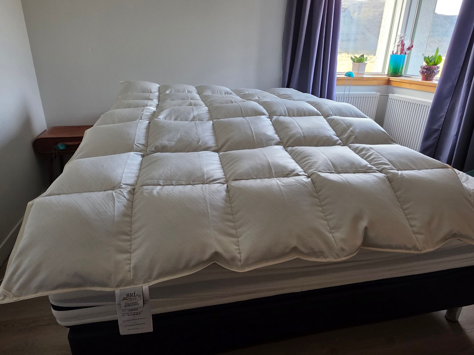 White quilted comforter and pillow on a bed, lit by natural light.
