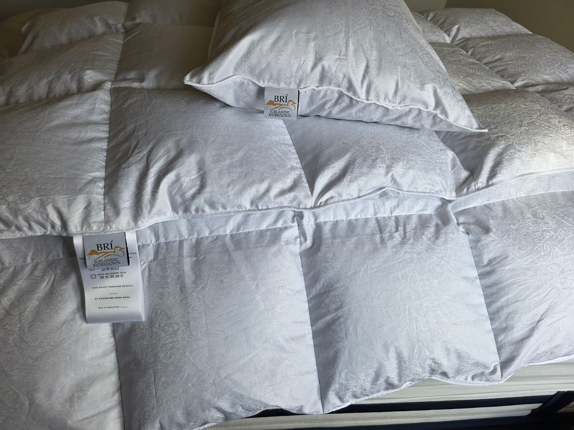White quilted comforter and pillow on a bed, with attached label visible.