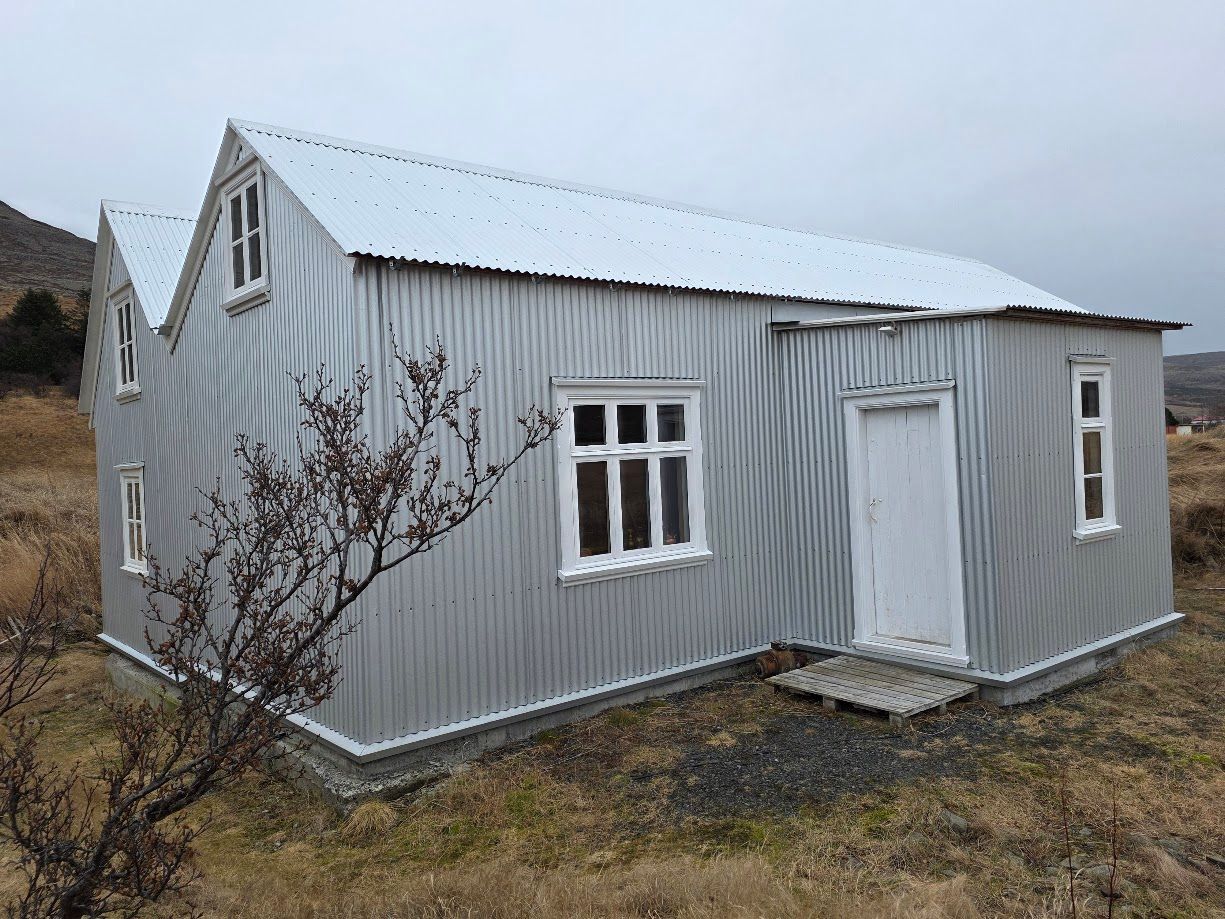 Two people wrapped in a white blanket, smiling, in front of a painting. Blue wall, wooden table.