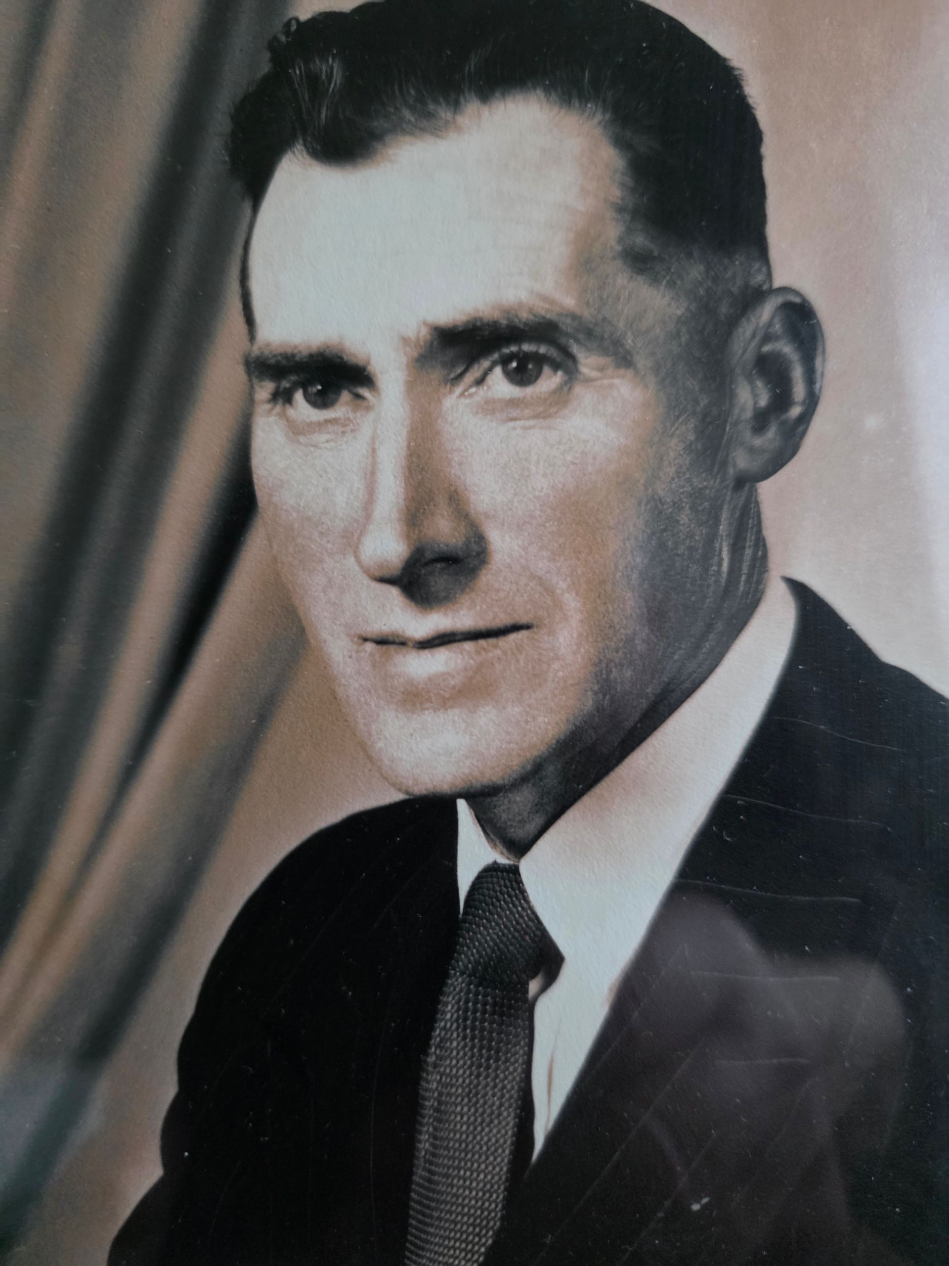 Two people wrapped in a white blanket, smiling, in front of a painting. Blue wall, wooden table.