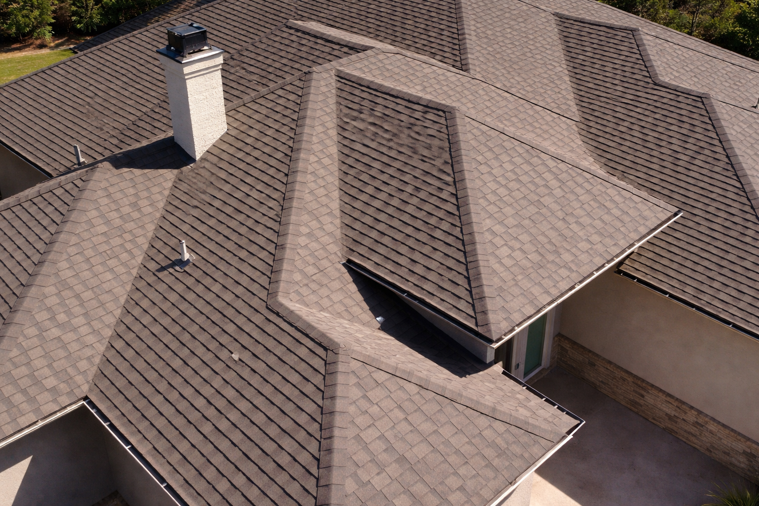 A high-angle view of a brown shingled roof with multiple gables and a white chimney.