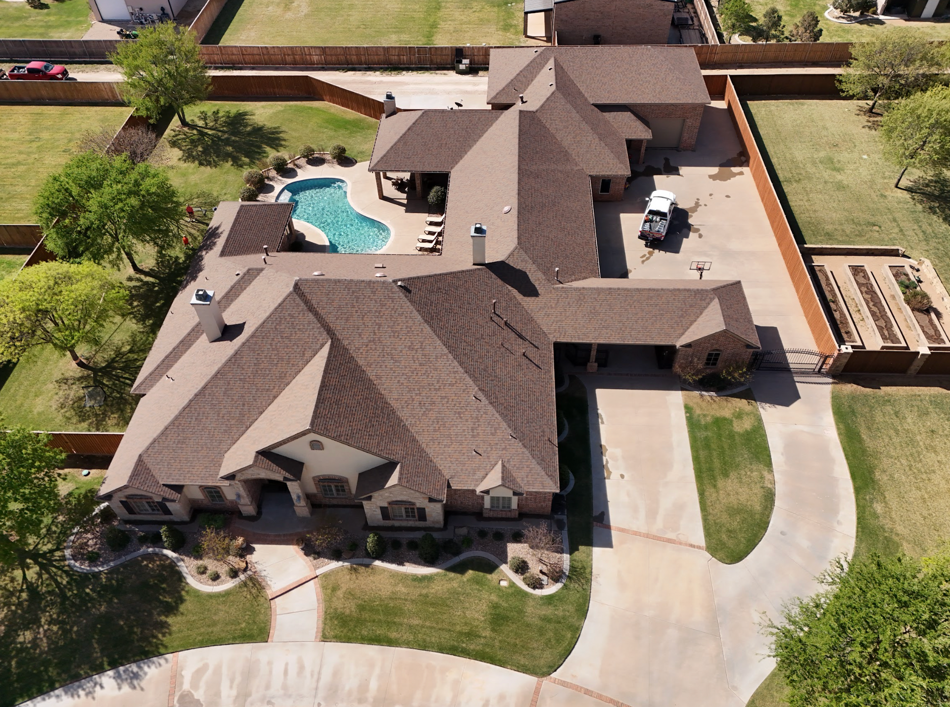 A high-angle view of a brown shingled roof with multiple gables and a white chimney.