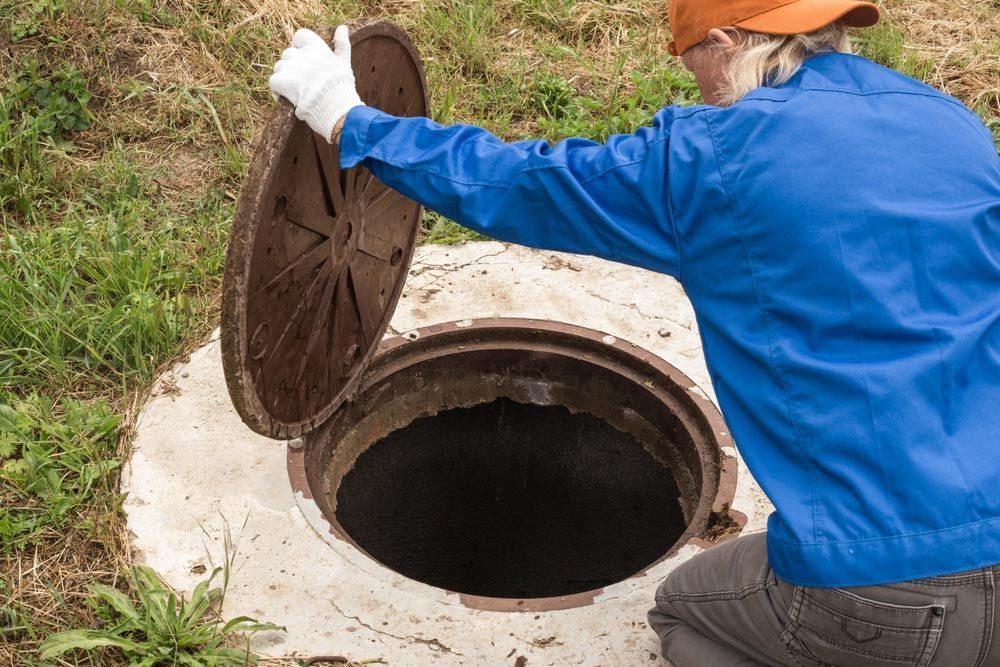 A Man is Kneeling Down to Open a Manhole Cover — Tony Brown Plumbing & Gas Services in South Grafton, NSW