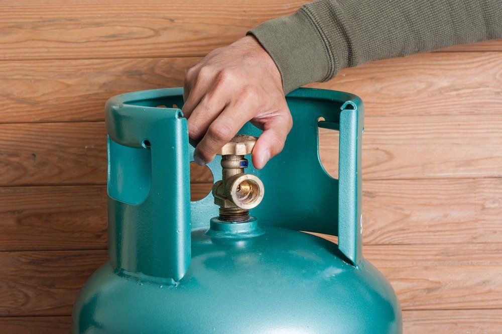 A Person is Plugging a Propane Tank Into a Wooden Wall — Tony Brown Plumbing & Gas Services in South Grafton, NSW
