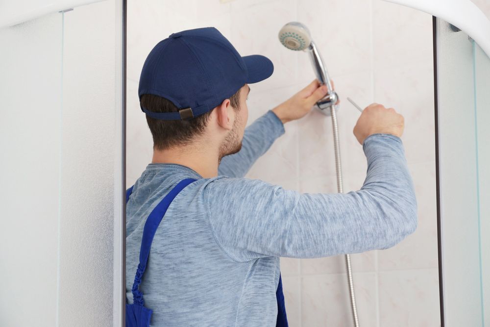 A Man is Fixing a Shower Head in a Bathroom — Tony Brown Plumbing & Gas Services in South Grafton, NSW