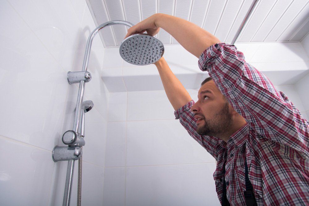 A Man is Fixing a Shower Head in a Bathroom — Tony Brown Plumbing & Gas Services in South Grafton, NSW