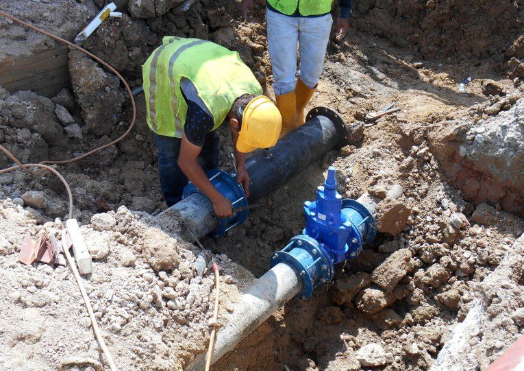 A Man in a Yellow Hard Hat is Working on a Pipe in the Dirt  — Tony Brown Plumbing & Gas Services in Woolgoolga, NSW