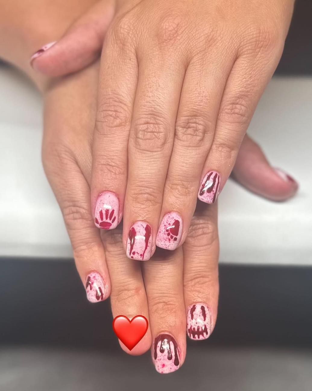 A close up of a woman 's nails with a red heart on her finger.