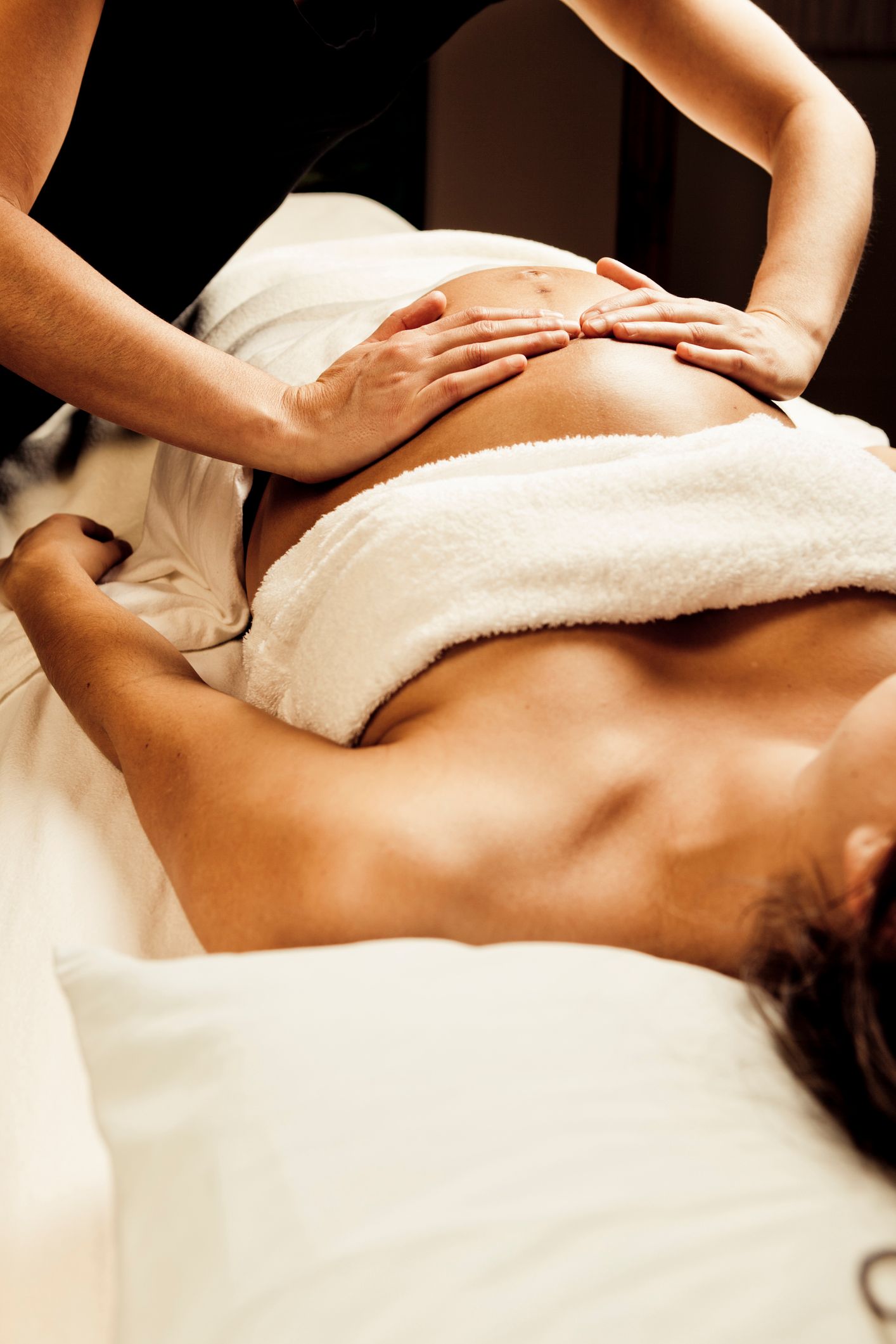 Person receiving a belly massage, lying on a massage table. Hands of another person are on their belly.