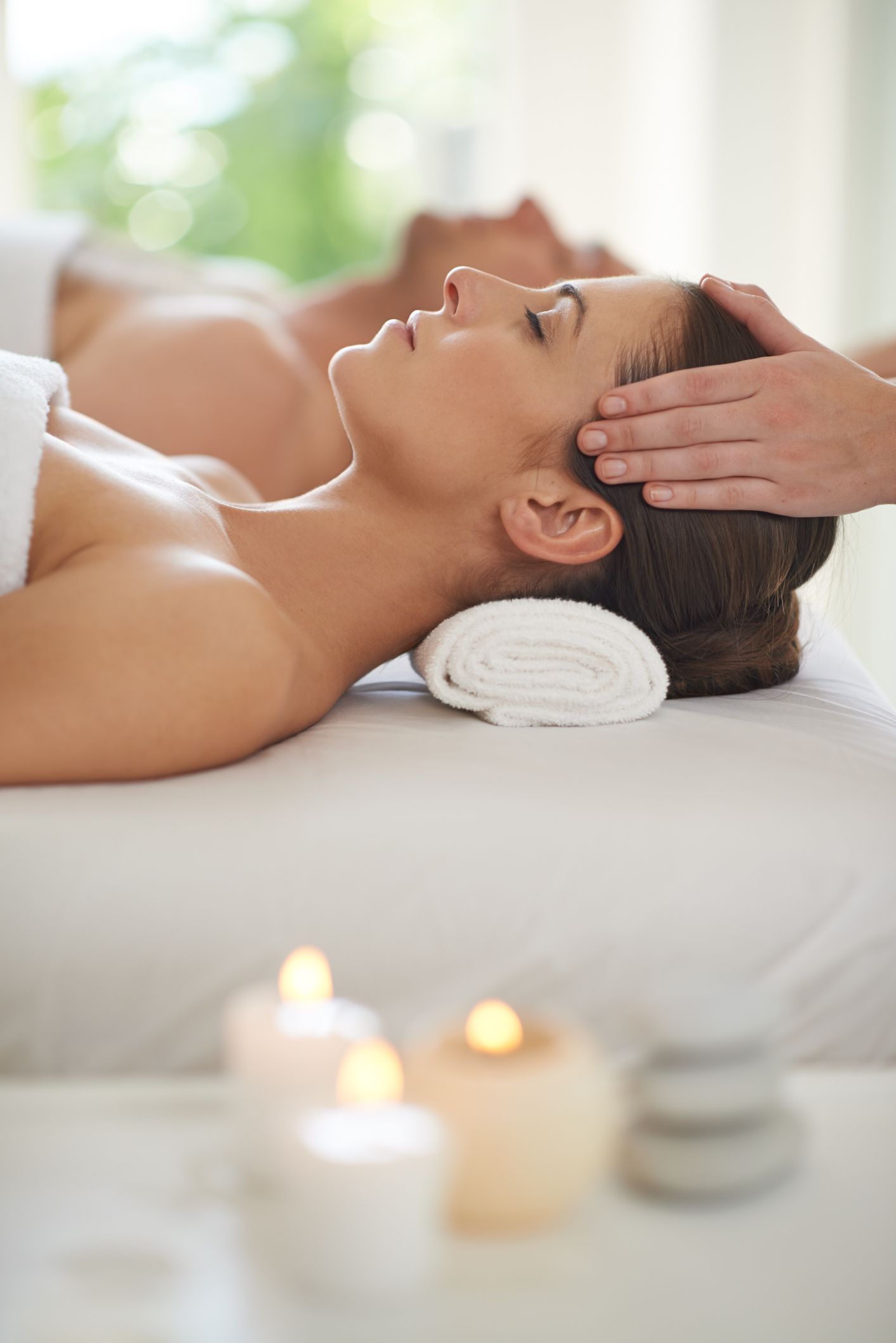 Woman receiving a head massage in a spa, lying on a massage table with lit candles nearby.